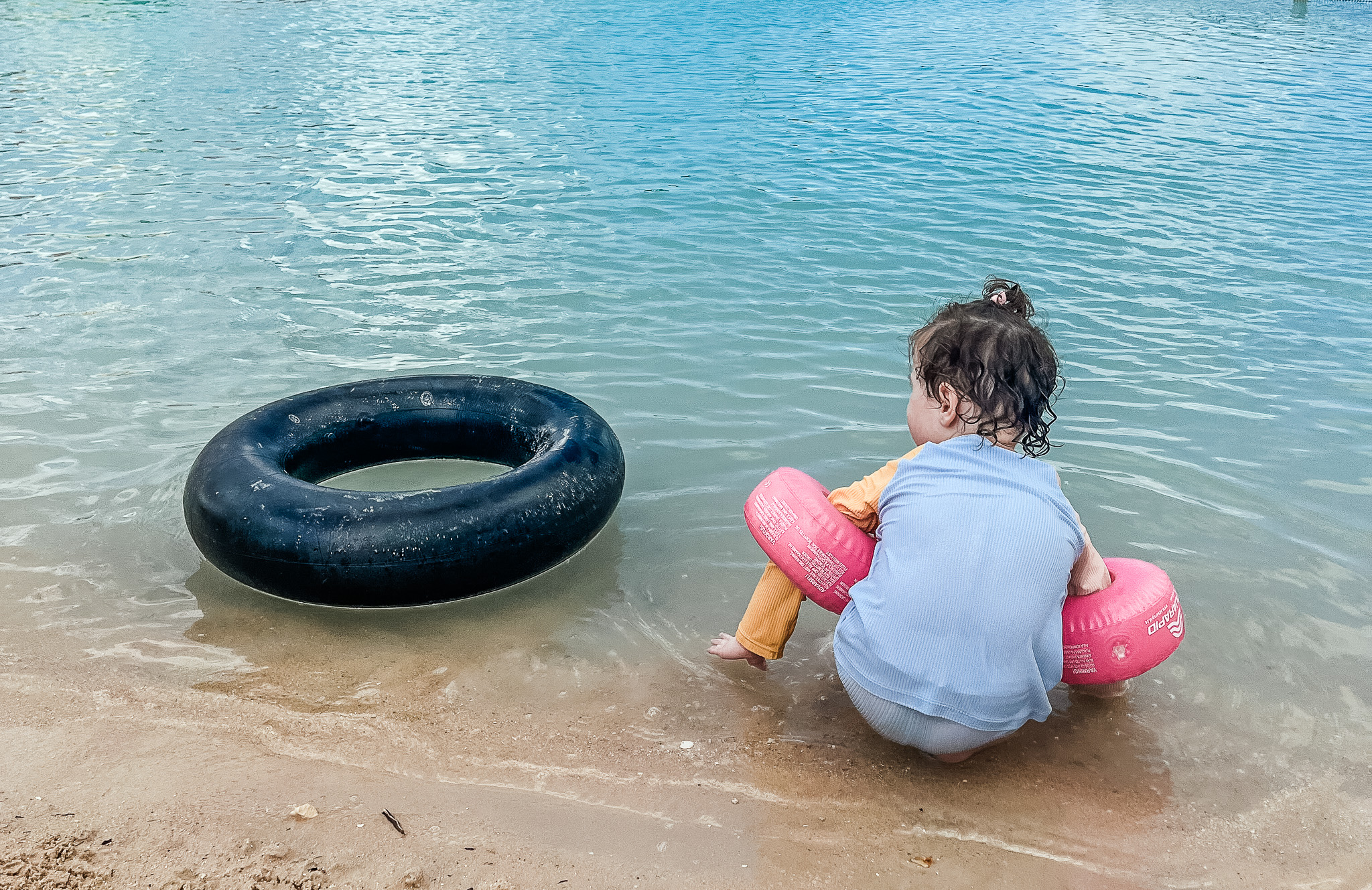 Peuter aan de rand van het water met een zwarte zwemband er naast